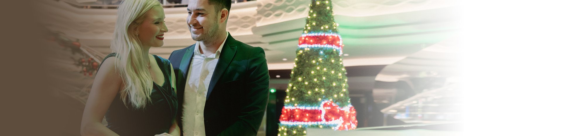 A couple standing near a decorated Christmas tree aboard a cruise ship | MSC Cruises A couple standing near a decorated Christmas tree aboard a cruise ship | MSC Cruises