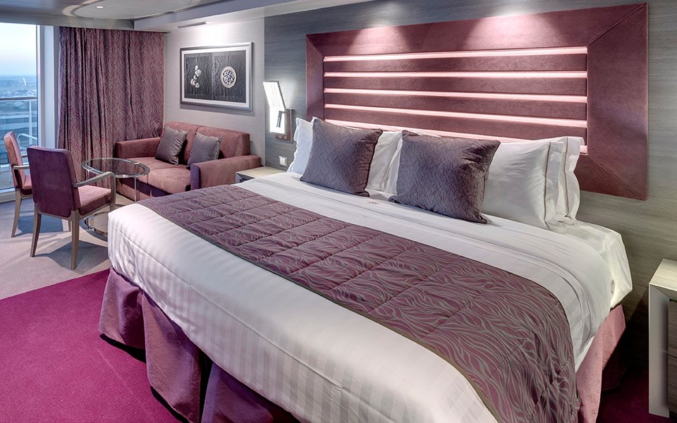 Elegant cruise ship suite with king-size bed, seating area, and balcony view | MSC Cruises